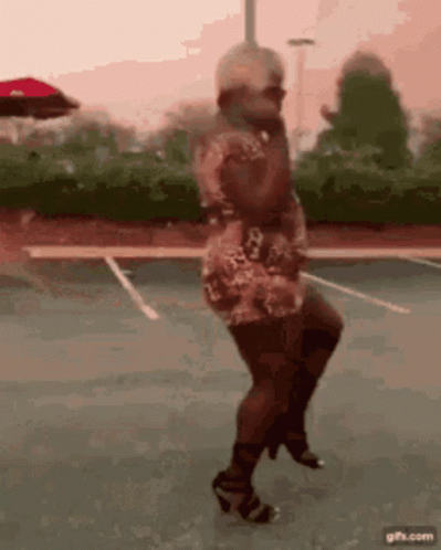 A Woman In A Dress And Heels Is Dancing On A Parking Lot . GIF