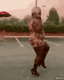 A Woman In A Dress And High Heels Is Dancing On A Parking Lot . GIF