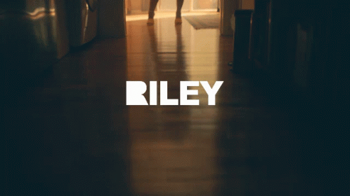 A Woman In A Dress Is Standing In A Hallway With The Word Riley On The Bottom GIF