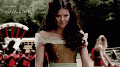 A Woman In A Dress Is Standing In Front Of A Crowd And The Words Made With Reface App Are On The Bottom Of The Screen GIF