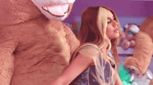A Woman In A Dress Is Standing Next To A Stuffed Animal GIF
