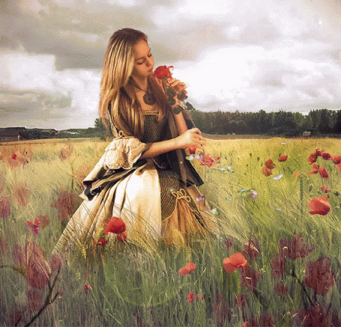A Woman In A Dress Smells A Rose In A Field GIF