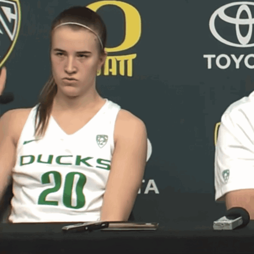 A Woman In A Ducks Jersey Sits At A Desk GIF