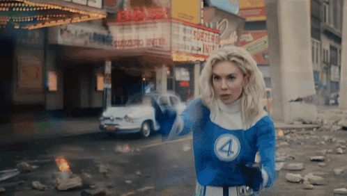 A Woman In A Fantastic Four Costume Stands In Front Of A Theatre GIF