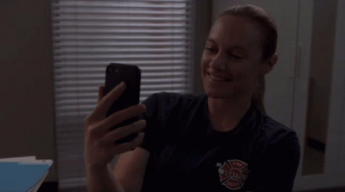 A Woman In A Firefighter Uniform Is Taking A Selfie With Her Cell Phone GIF