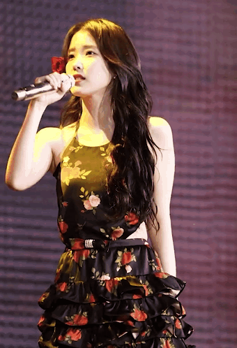 A Woman In A Floral Dress Holds A Microphone In Her Hand GIF