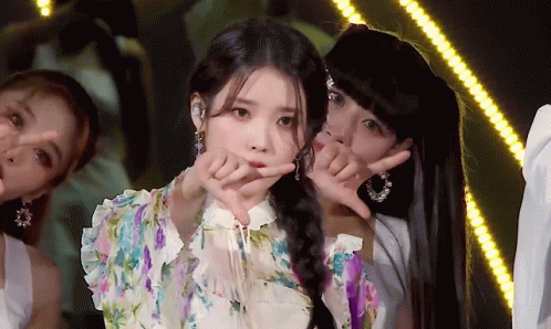 A Woman In A Floral Dress Is Making A Heart Shape With Her Fingers GIF