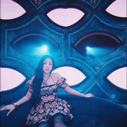 A Woman In A Floral Dress Is Sitting In Front Of A Wall With Eyes GIF
