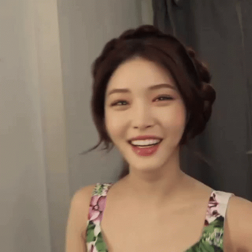 A Woman In A Floral Dress Is Smiling And Looking At The Camera In A Room . GIF