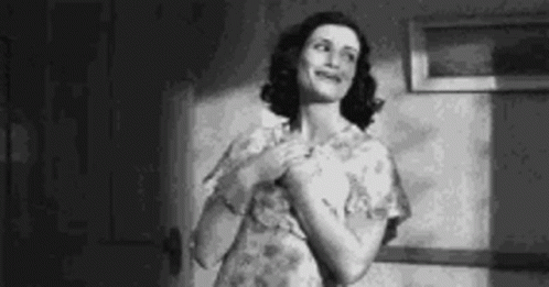 A Woman In A Floral Dress Is Standing In A Room And Smiling . GIF