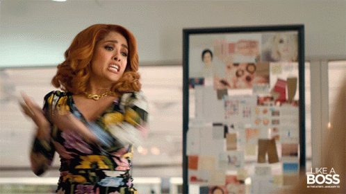 A Woman In A Floral Dress Is Standing In Front Of A Framed Picture That Says Like A Boss GIF
