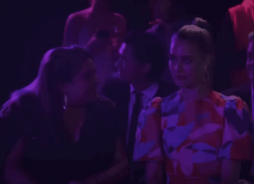 A Woman In A Floral Dress Talks To A Man In A Suit GIF