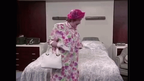 A Woman In A Floral Robe And Pink Hat Is Standing In Front Of A Bed In A Hospital Room . GIF