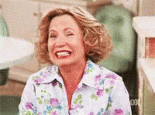 A Woman In A Floral Shirt Is Laughing While Sitting Down . GIF