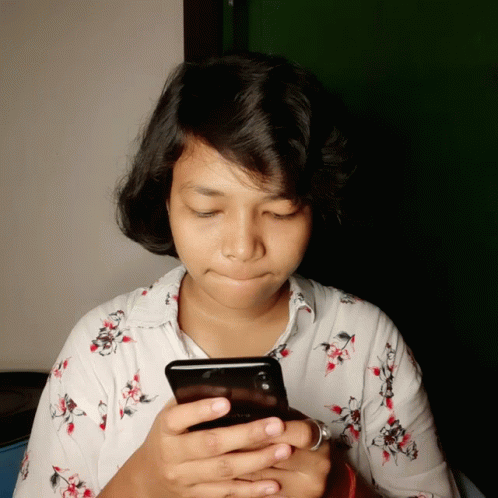 A Woman In A Floral Shirt Is Looking At A Cell Phone GIF