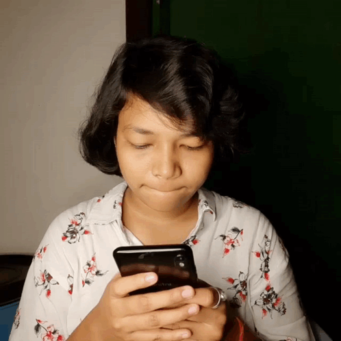 A Woman In A Floral Shirt Is Looking At Her Cell Phone GIF