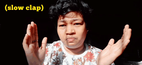 A Woman In A Floral Shirt Is Making A Funny Face With Her Hands Outstretched And The Words Slow Clap Below Her GIF