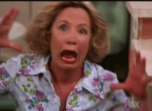 A Woman In A Floral Shirt Is Making A Funny Face With Her Mouth Open And Her Hands Outstretched . GIF