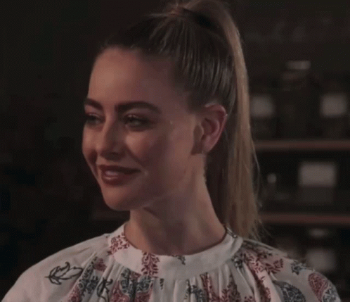 A Woman In A Floral Shirt Is Smiling And Looking At The Camera GIF