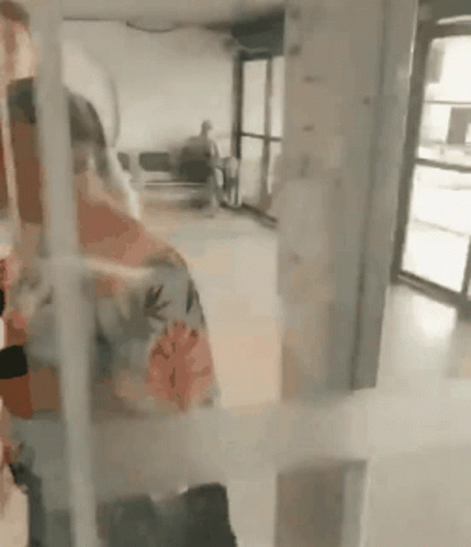 A Woman In A Floral Shirt Is Standing In A Room With A Glass Door . GIF