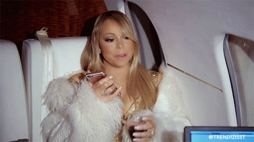 A Woman In A Fur Coat Is Sitting In Front Of A Screen That Says Trendizisst On It GIF