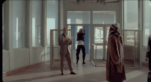 A Woman In A Fur Coat Stands In Front Of A Door That Says Tm GIF