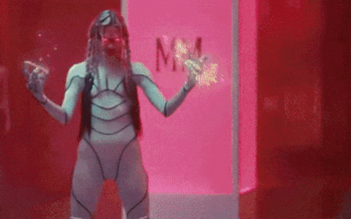 A Woman In A Futuristic Costume Is Standing In Front Of A Pink Box With The Word Mm On It . GIF