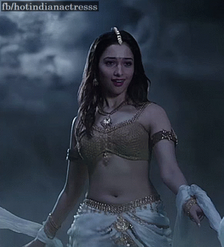 A Woman In A Gold Bra And White Pants Is Dancing In The Dark . GIF