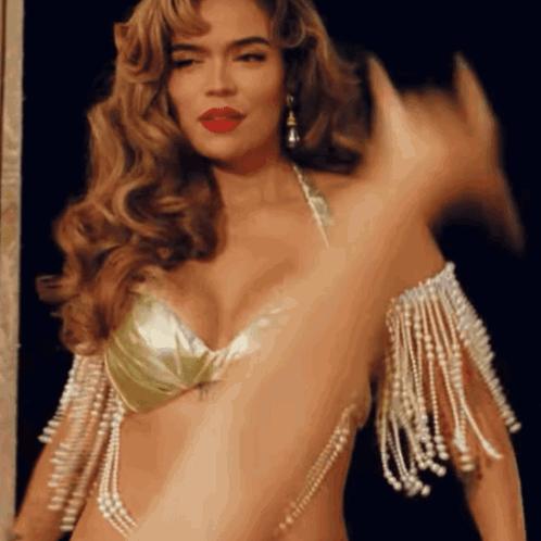 A Woman In A Gold Bra With Pearls On The Sleeves Is Dancing GIF