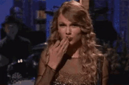 A Woman In A Gold Dress Is Blowing A Kiss . GIF
