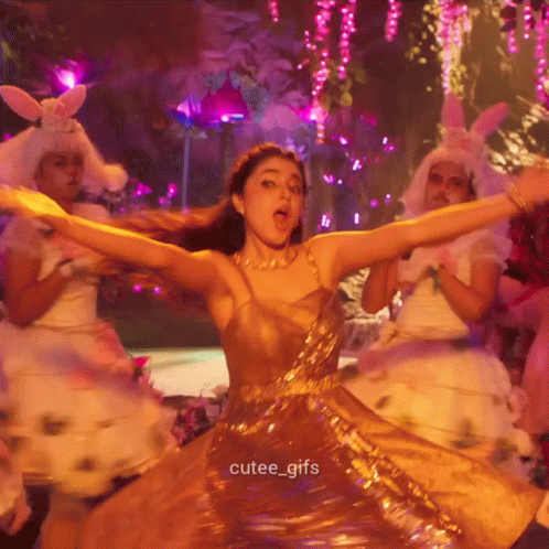 A Woman In A Gold Dress Is Dancing With Her Arms Outstretched And The Caption Cutee_gifs Is Below Her GIF