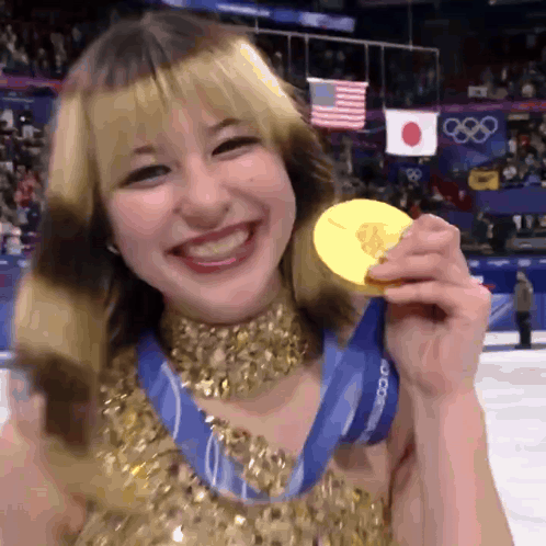 A Woman In A Gold Dress Is Holding A Gold Medal And Smiling GIF