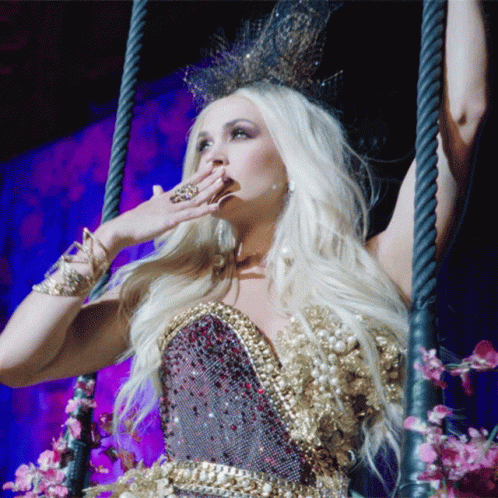 A Woman In A Gold Dress Is Holding Her Hand To Her Face GIF