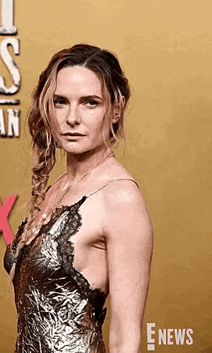 A Woman In A Gold Dress Is Standing On A Red Carpet And Looking At The Camera . GIF
