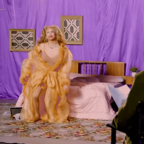 a woman in a gold robe is standing in a bedroom with purple curtains