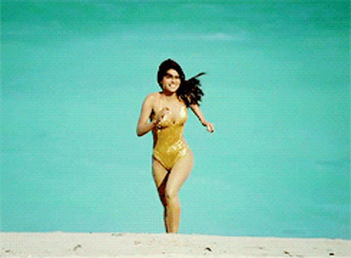 A Woman In A Gold Swimsuit Is Running On A Beach GIF