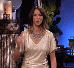 A Woman In A Gold Top And Silver Necklace Holds A Glass GIF
