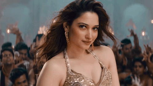 A Woman In A Gold Top Stands In Front Of A Crowd Of People GIF