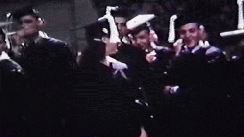 A Woman In A Graduation Cap And Gown Is Smiling In Front Of A Crowd Of People . GIF