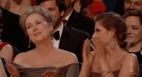 A Woman In A Gray Dress Is Applauding Another Woman GIF