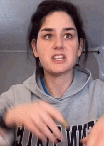 A Woman In A Gray Hoodie Is Making A Funny Face While Holding Her Hands Out . GIF