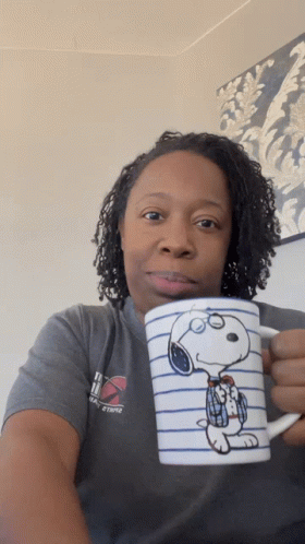 A Woman In A Gray Shirt Holds A Snoopy Coffee Mug GIF
