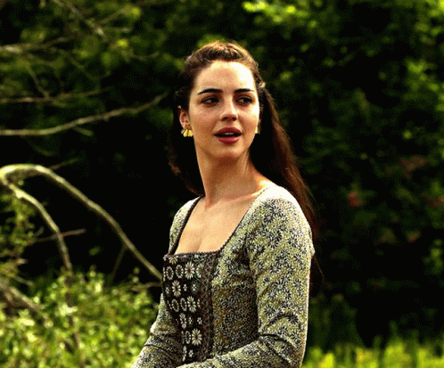 A Woman In A Green And Black Dress Is Standing In A Field GIF
