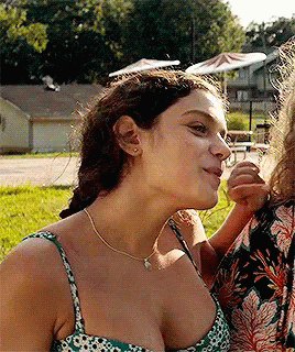 A Woman In A Green And White Floral Tank Top Looks Down At Something GIF