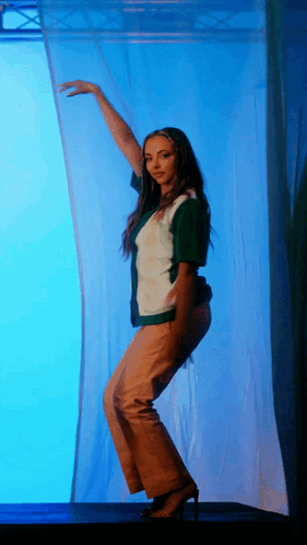 A Woman In A Green And White Shirt Is Dancing In Front Of A Blue Background GIF