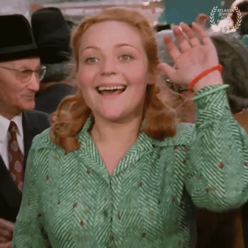 A Woman In A Green And White Shirt Is Smiling And Waving GIF