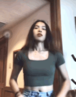 A Woman In A Green Crop Top And Shorts Is Standing In A Room . GIF