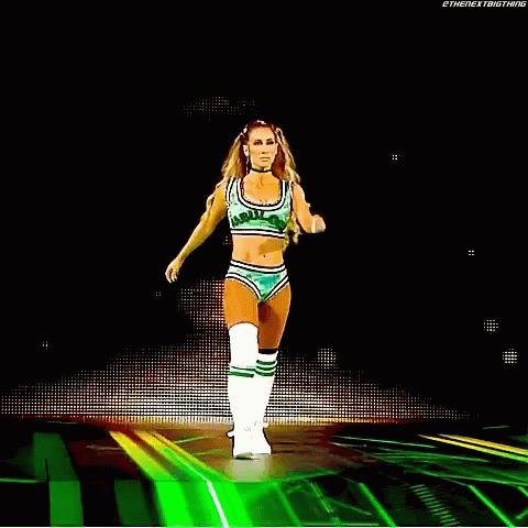A Woman In A Green Crop Top And Shorts Is Walking On A Stage . GIF