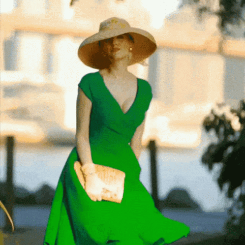 A Woman In A Green Dress And Straw Hat Holds A Clutch GIF