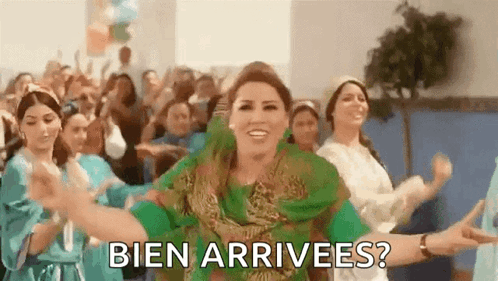 A Woman In A Green Dress Is Dancing In Front Of A Crowd With The Words Bien Arrivees ? Written Below Her . GIF